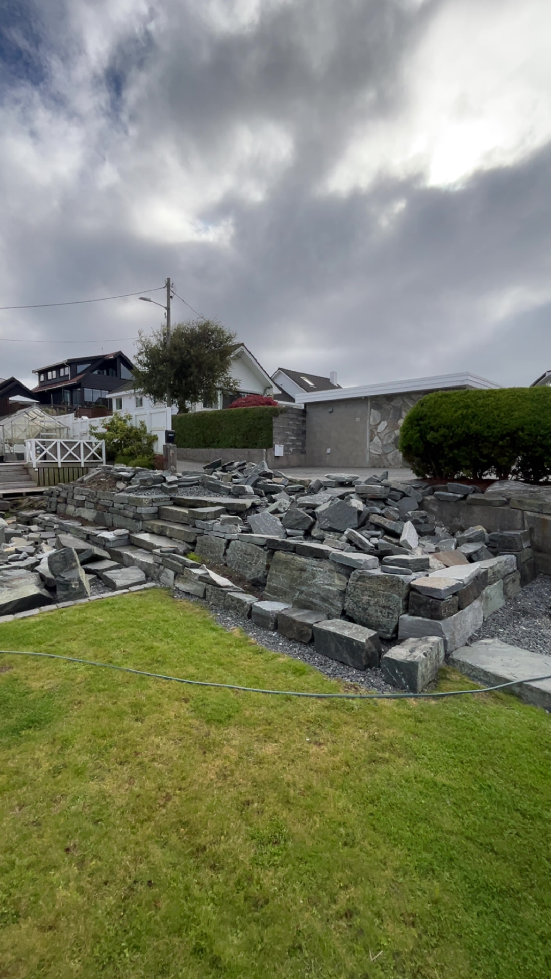 Hagen med halvferdig natursteinsmur og stein spredt utover før ferdigstilling
