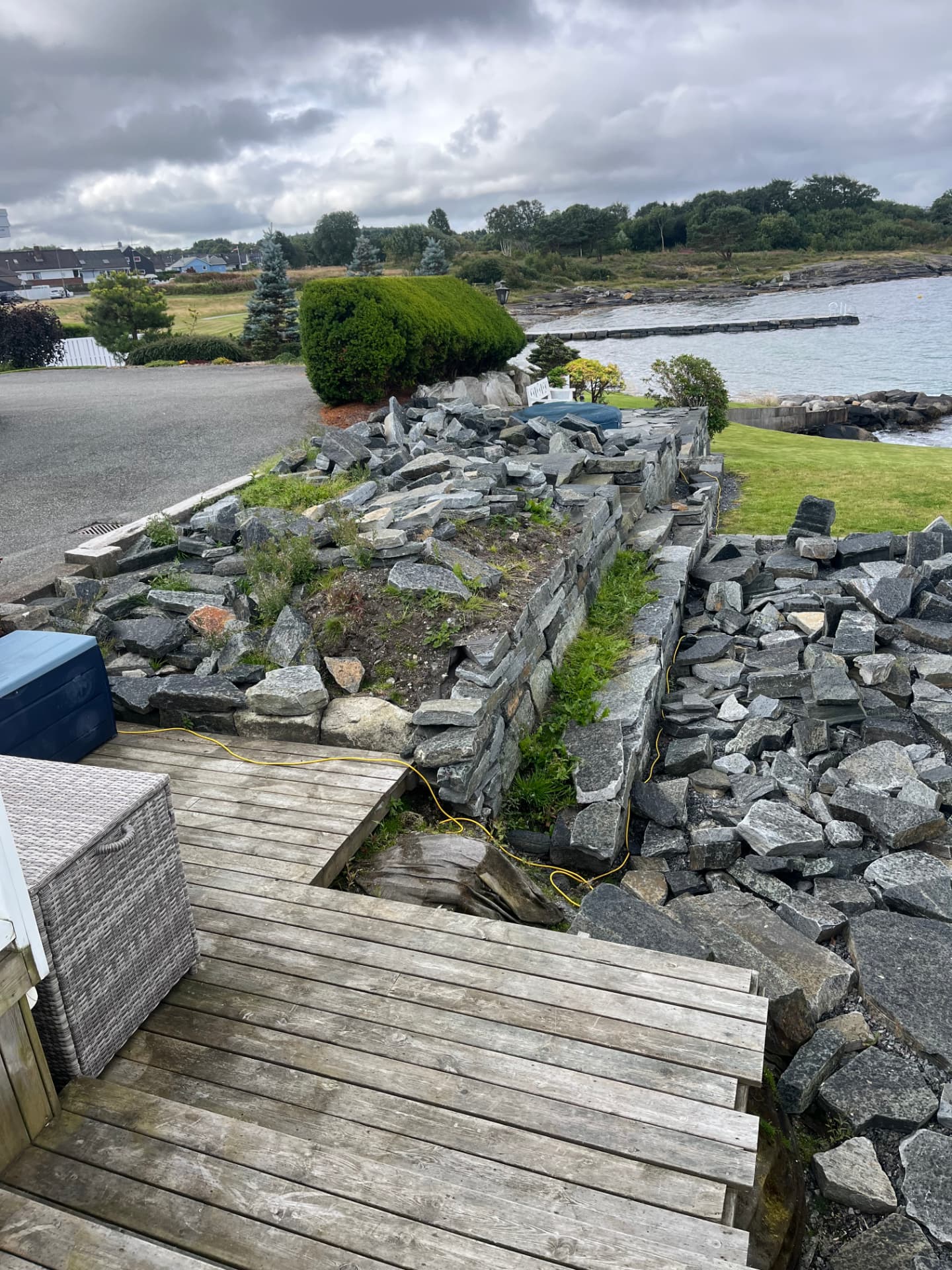 Uteområdet sett fra terrassen før arbeidet, med delvis oppført natursteinsmur og løse steiner