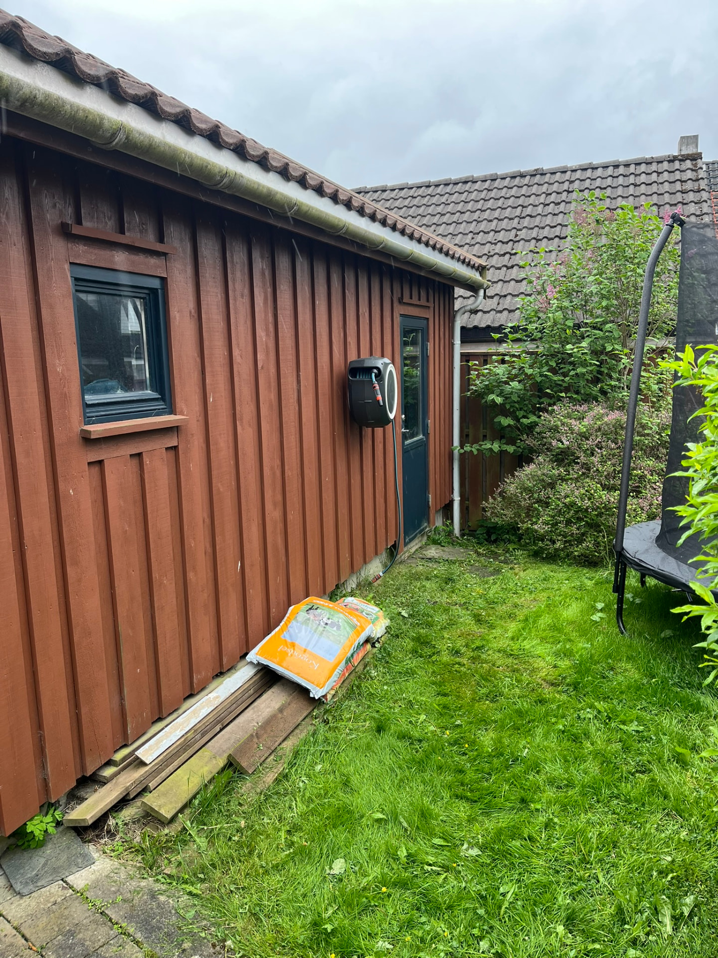 Gressplenen og veggen der uteboden skulle bygges, med materialer liggende langs veggen