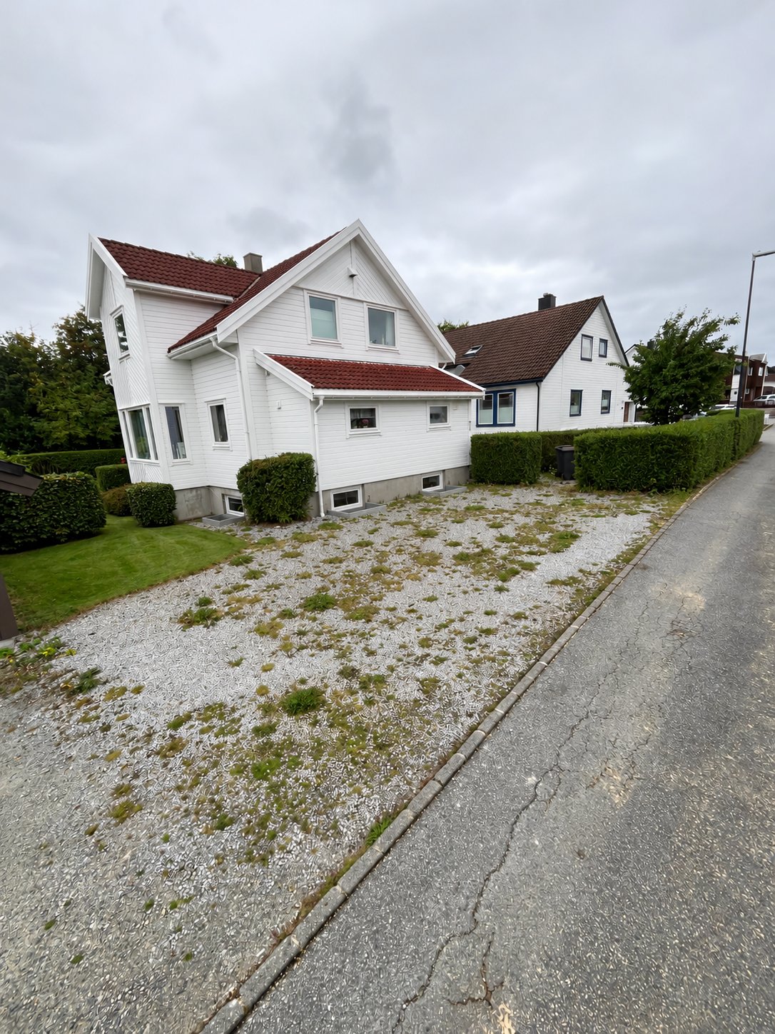 Uteområdet sett fra veien før arbeidet, med grusflate og ugress foran huset
