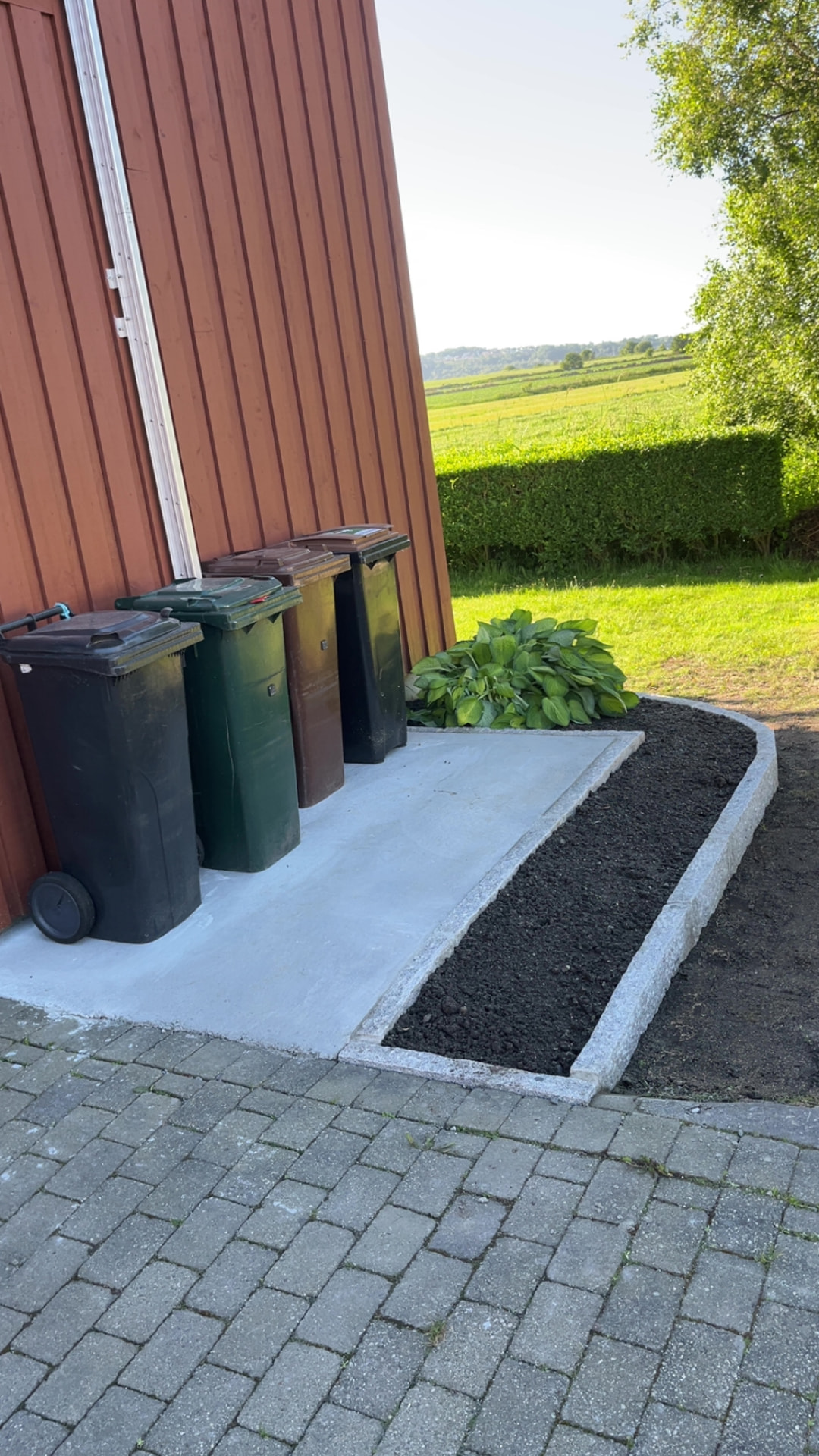 Søppeldunkene på støpt plate med nytt bed og kantstein ved siden av