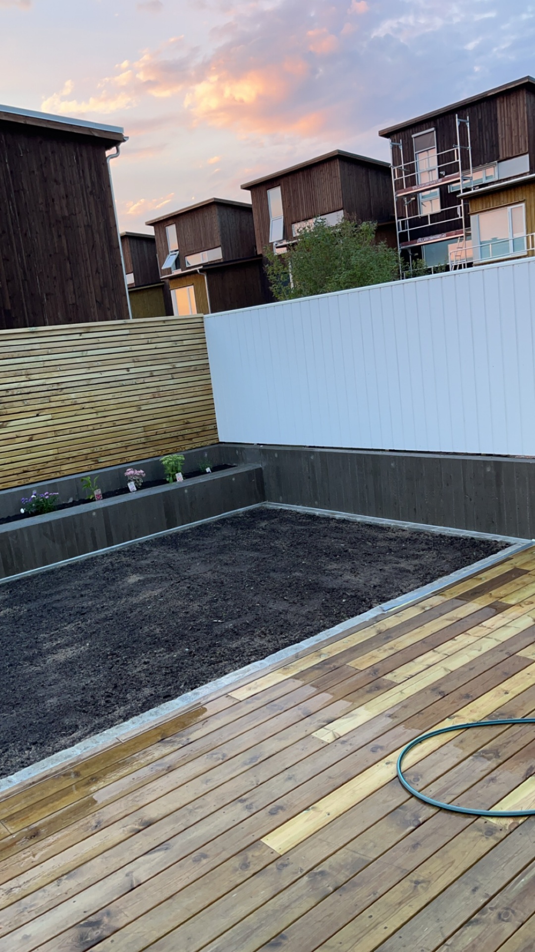 Ferdig uteplass med terrasse, plantekasse og skjermvegg i skumring